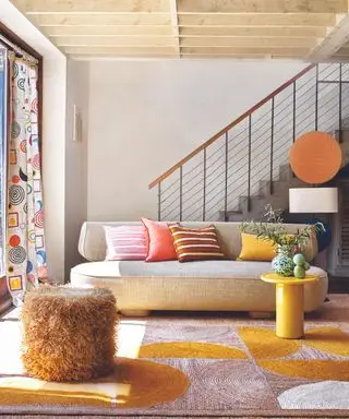 Sofá gris, alfombra amarilla, rosa y blanca, esponjoso reposapiés naranja