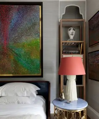 Dormitorio decorativo con una mezcla de obras de arte y una lámpara de mesita de noche de gran tamaño con pantalla rosa.