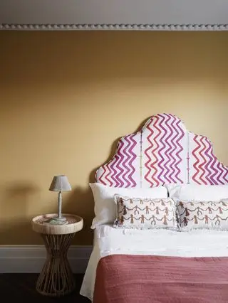 Dormitorio amarillo con cabecera y cornisas.