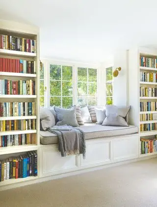 Biblioteca con asiento junto a la ventana y estanterías equipadas a ambos lados con vista al jardín