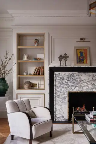 salón neutro con suelo de madera, chimenea de mármol, sillón y alcoba