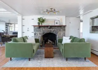 Sala com sofás verdes voltados, lareira e piso de madeira