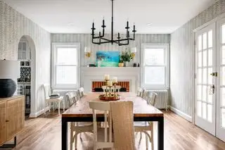 Sala de jantar com mesa de madeira, cadeiras pintadas, papel de parede estampado cinza e piso de madeira