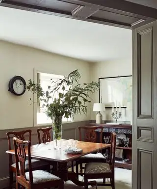 Traditionelles Esszimmer mit grün gestrichener Wand- und Deckenverkleidung, dunklem Esstisch mit vier passenden Stühlen, Pflanze in der Mitte des Tisches, Holzschrank mit Tischlampe und Kandelaber sowie gerahmter Karte