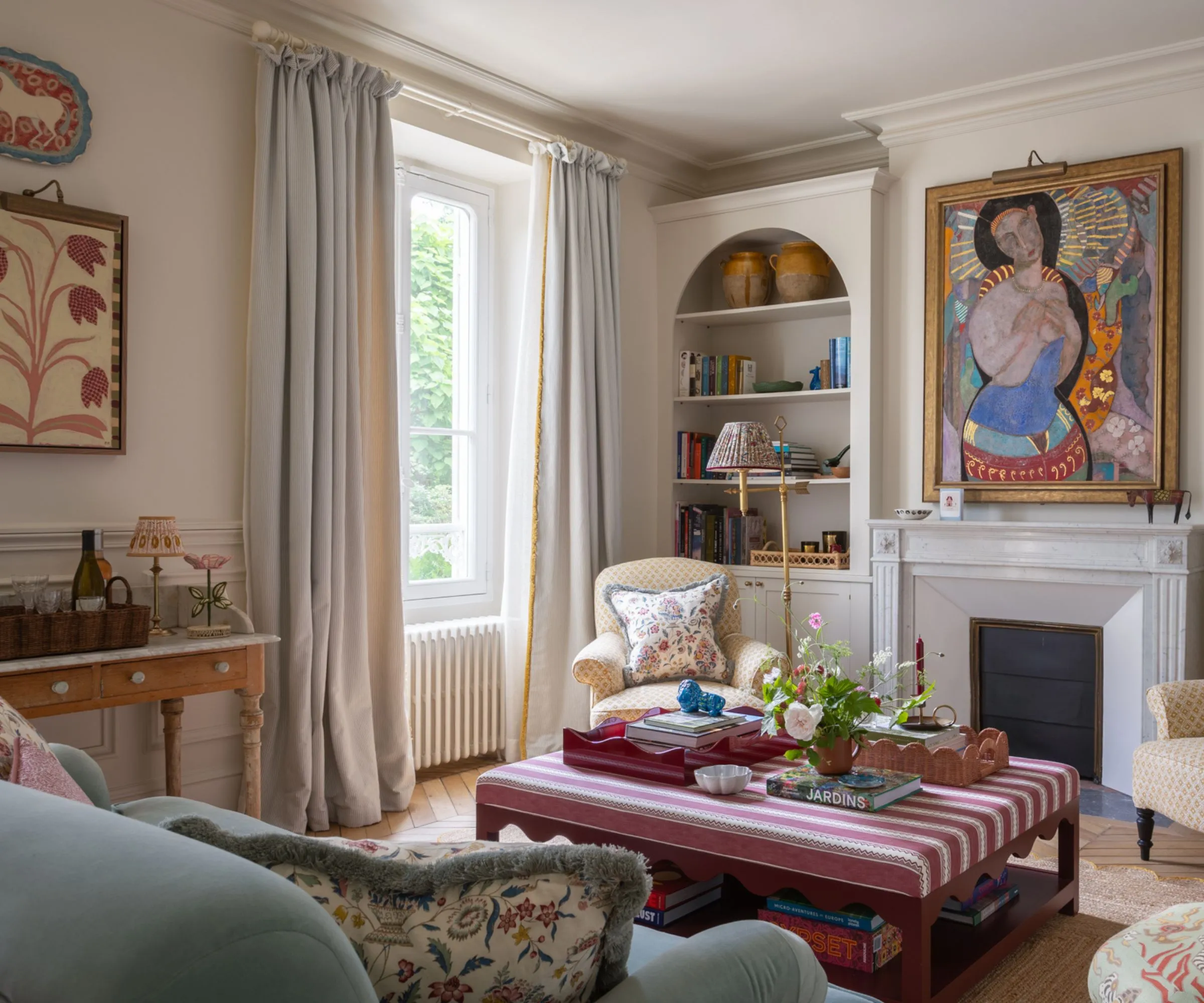 tradičná obývacia izba s eklektickým mixom nábytkových potlačí a farieb krb s veľkými umeleckými dielami a pruhovaným otomanom' loading='lazy' title=