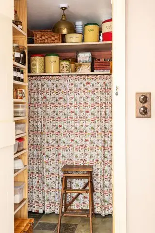 Despensa llena de latas antiguas y parcialmente cubierta por una cortina floral vintage.