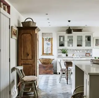 Cocina blanca con cómoda de madera antigua y cálido suelo de parquet.