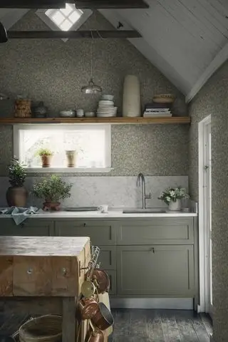 Muebles de cocina verde salvia y papel pintado estampado. Salpicadero de mármol y encimeras con bloques de vutchers recuperados y estantes abiertos de madera que exhiben vasijas y cerámicas.