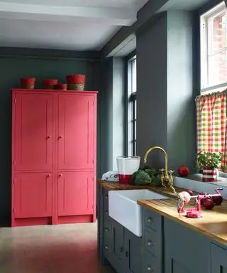 Et mørkegrå kjøkkenfargevalg med korallrødt malt pantry og gingham persienner.