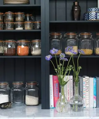 Et nærbilde av svarte åpne hyller med matkrukker, bøker og blomster