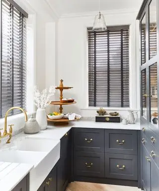 Cozinha moderna em branco e azul arca, venezianas em marrom escuro, pingente de vidro suspenso, bancadas decoradas com utensílios de cozinha e acessórios