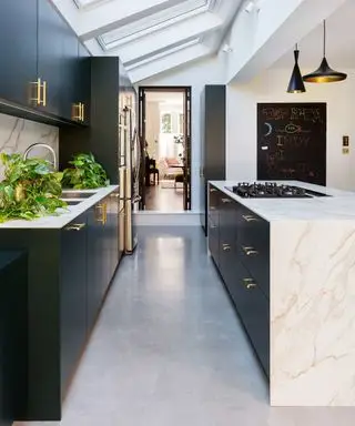 você pode colocar uma ilha em uma cozinha de galé, cozinha de galé preta e mármore em extensão, claraboias, vista para a sala de estar, quadro-negro, luminária pendente, piso cinza, fogão na ilha