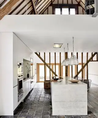 Elegante cocina blanca Roundhouse en un granero histórico con vigas y suelo de piedra adoquinada