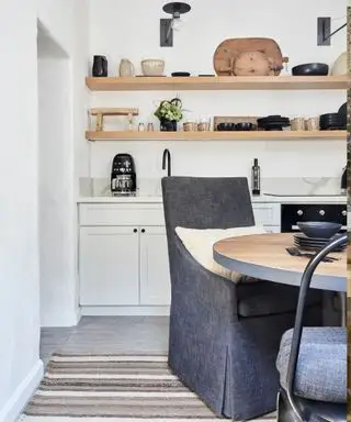 Cocina rústica moderna con estanterías abiertas, armarios blancos, mesa de comedor circular de madera y sillas de lino