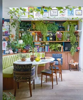 Spazio cucina-sala da pranzo massimalista, panche, tavolo da pranzo rotondo in marmo a forma di tulipano, parete della galleria, lucernario, piante decorate attorno al tavolo, pavimento in legno