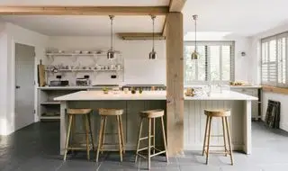Hvitt kjøkken med trebjelker, åpne hyller og trekrakker på en øy malt med off-white aksenter.