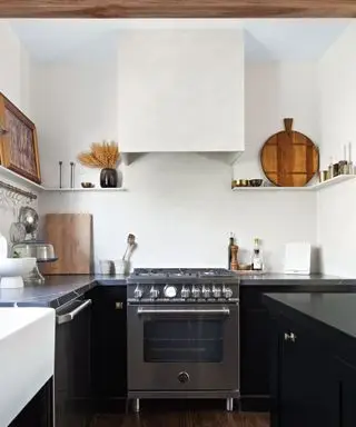 Pequeña cocina negra brillante con electrodomésticos de acero inoxidable y campana extractora de yeso.