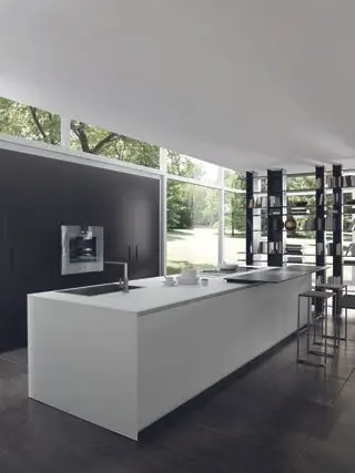 Elegantní, moderní kuchyně s bílým kuchyňským ostrůvkem a tmavými dřevěnými podlahami a skříňkami, které jsou v jednom se stěnou.