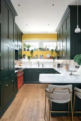 Cucina con mobili verdi e penisola, pavimento in legno e parete gialla