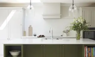 Grün-weiße Küche mit grün gestrichener Kücheninsel, weißen Schränken, Spüle in der Kücheninsel, Hängeleuchten aus Glas