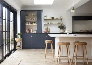 Blau-weiße Küche mit geschlossenem Schrank, offenen Regalen, Kochinsel, weißen Arbeitsplatten, Fischgrätenboden und Holzhockern
