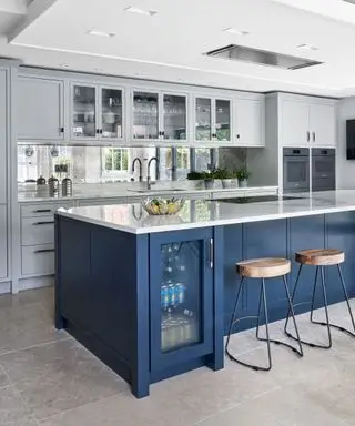 Cucina con parete piastrellata a specchio, pareti bianche e isola cucina blu scuro con frigorifero integrato e sgabelli da bar