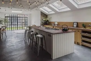 Un'isola da cucina rivestita in legno con sgabelli da bar rustici in metallo e lucine sul soffitto.