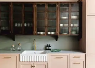 Mobili da cucina verniciati rosa pallido con armadi in legno sopra e ripiani grigi.