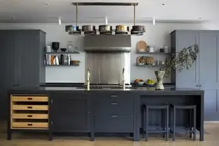 Mobili da cucina verniciati di nero con dispensa grigio scuro, piano cottura e alzatina cromati e illuminazione d'effetto.