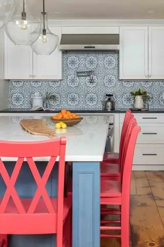 Mobili da cucina bianchi con bancone per la colazione verniciato blu-grigio e sedie rosso corallo brillante.