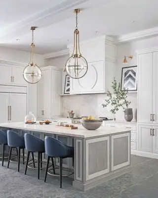 Una grande isola da cucina con mobili da cucina dipinti di grigio e bianco con posti a sedere blu e illuminazione a sospensione d'effetto.
