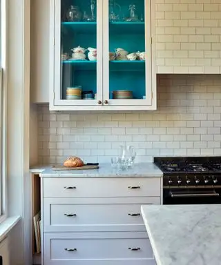 Cocina estilo shaker de color rosa pálido con azulejos blancos y un mueble de pared vidriado.