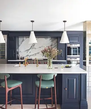 Cucina componibile blu a pianta aperta con piani di lavoro bianchi, isola cucina e sgabelli da bar verdi di metà secolo. Alzatina in marmo.