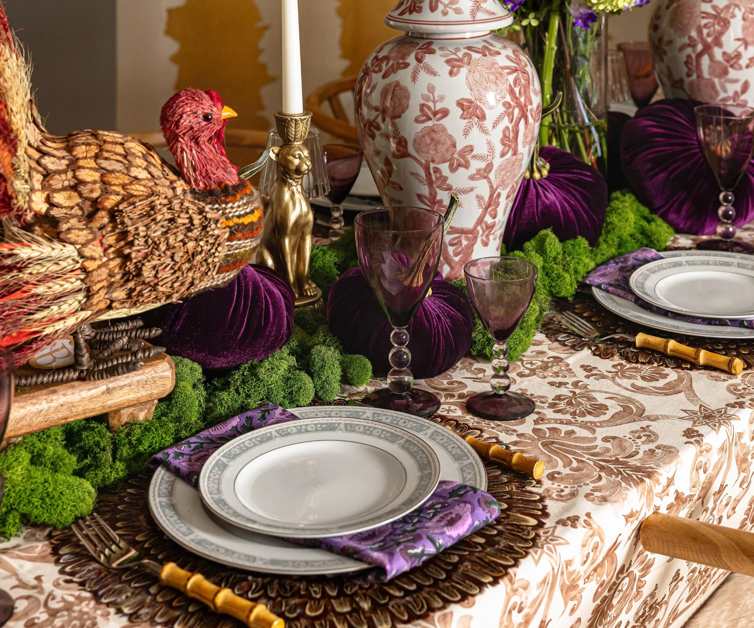 Thanksgiving -bordbillede med et hvidt og brunt mønstret duge -rottingopladerplader og et stort kalkun midtpunkt med mos- og ingefærkrukker' loading='lazy' title=