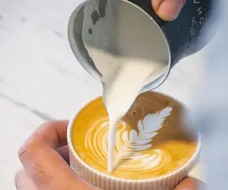 Barista som heller melk i espressokaffe for å lage cappuccino, latte art