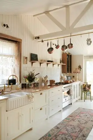 off-white kjøkken i vintage stil med shiplap vegger, hvitmalt gulv, vintage teppe, marmor benkeplate, butler vask, flislagt backsplash, åpne hyller, hengende redskaper