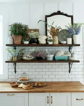 åpne hyller med blomster i keramikk og et speil over hvitt kjøkkenskap med benkeplate i tre