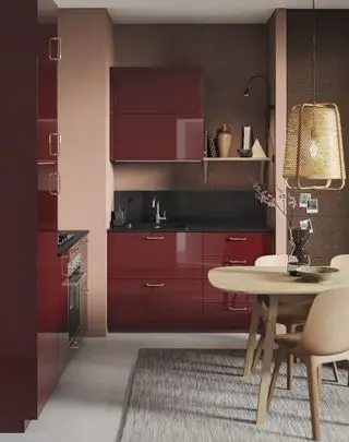 Et lite rødt kjøkken med blanke skap, dempede rosa og brune vegger og bleke tremøbler.