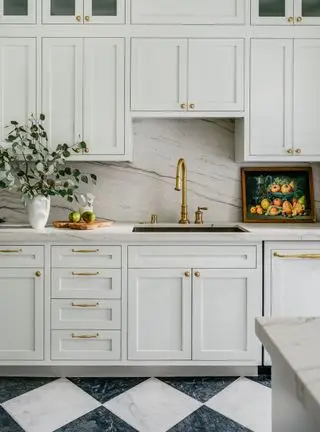 Cocina blanca con protector contra salpicaduras de mármol y herrajes dorados.