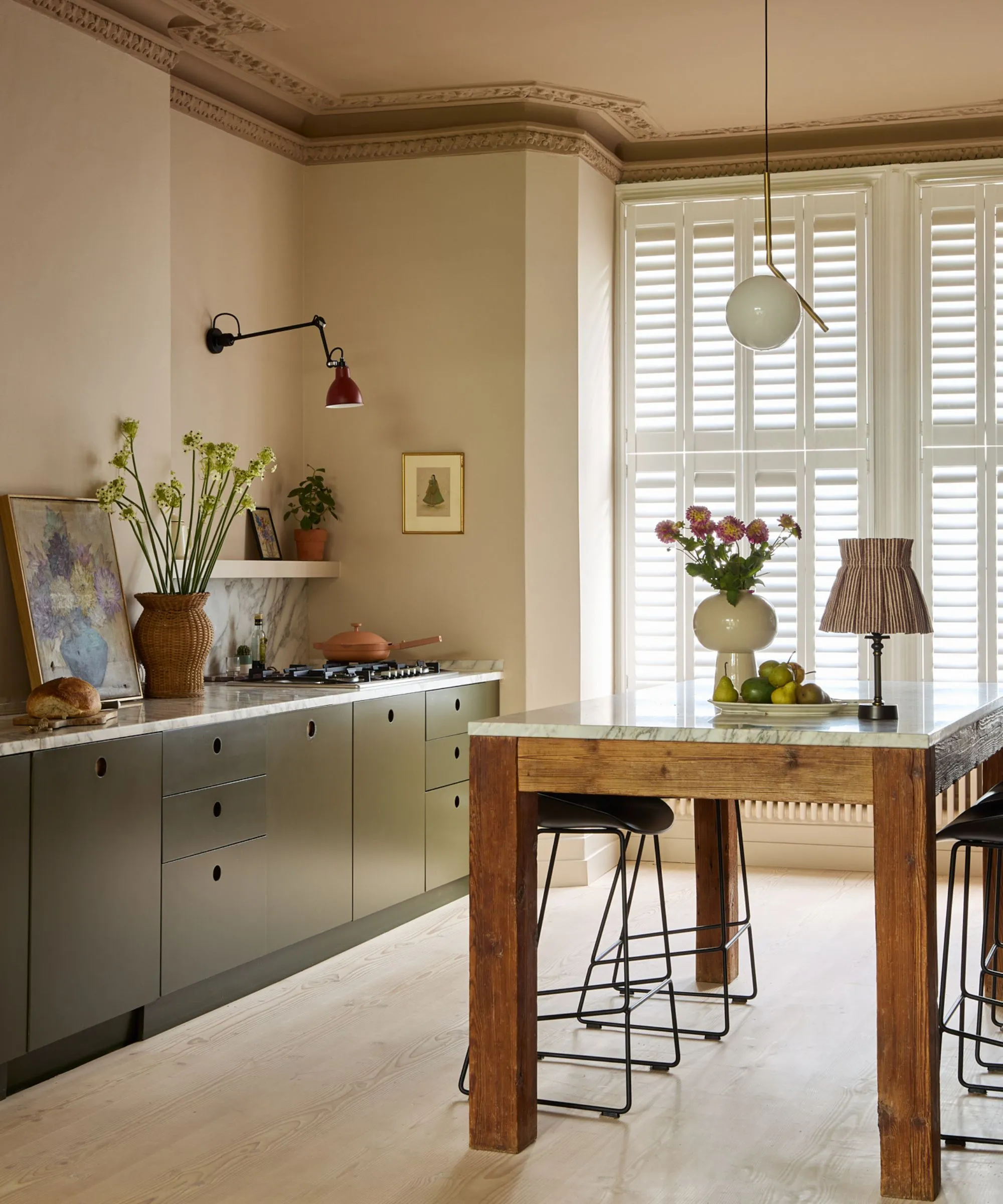 Une cuisine aux tons chauds avec des armoires vert foncé, des comptoirs en marbre et un îlot autoportant en bois' loading='lazy' title=