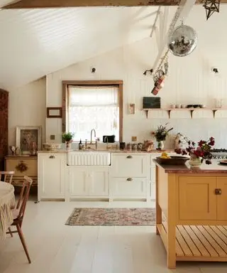 cómo diseñar una casa que se sienta como usted, cocina de estilo vintage con paredes traslapadas, piezas vintage, lámpara colgante con flecos, fregadero estriado, grifo de latón, isla mostaza, mesa de comedor, estanterías abiertas