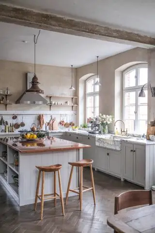 Eine Küche im Landhausstil mit Fischgrätenboden, einer großen Insel mit cremefarbenen Schränken und zwei Barhockern aus Holz