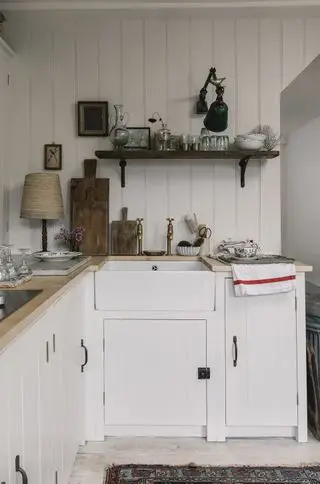 Eine weiße Küche im Landhausstil mit originalen Schränken und offenen Regalen über einem Waschbecken