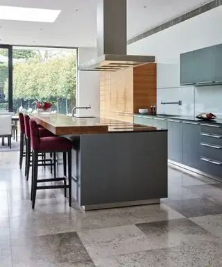Eine Küche mit grauen Granitbodenfliesen und einer großen Insel mit pflaumenfarbenen Barhockern