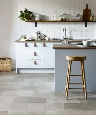 Küche mit grauem Vinylboden in Steinoptik, blaugrauer Kücheninsel, Küchenschränken und Arbeitsplatte aus weißem und dunklem Holz, Regalen aus dunklem Holz mit Küchenzubehör
