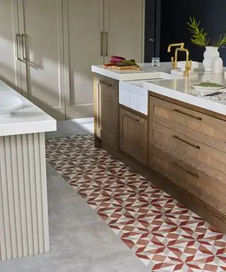Küche mit gemustertem Vinylfliesenboden, Kücheninsel aus dunklem Holz mit weißer Arbeitsplatte, beige gestrichene Küchenschränke