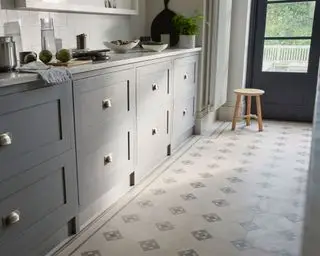 Küche mit Vinylboden mit Fliesenmuster, grauen Schränken, Arbeitsplatte aus weißem Marmor, weißen Fliesen, hellem Holzhocker