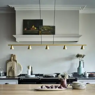 Design af en køkkenø med belysningsideer indarbejdet i form af en lang, cremefarvet pendel, i et hvidt køkkenskema.