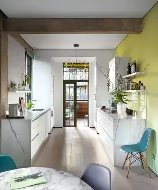 Una cocina de mármol con paredes amarillas, estanterías abiertas y sillas verde azulado.