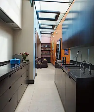 Una idea de cocina de galera negra en una habitación estrecha con paredes naranjas y tragaluces.